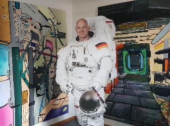 lebensgroßer Aufsteller Alexander Gerst im Raumanzug, im Hintergrund großflächige bunte Gemälde