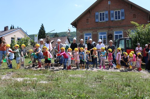 Kinder und Erwachsene mit Schaufeln und Helmen bei einem Spatenstich.